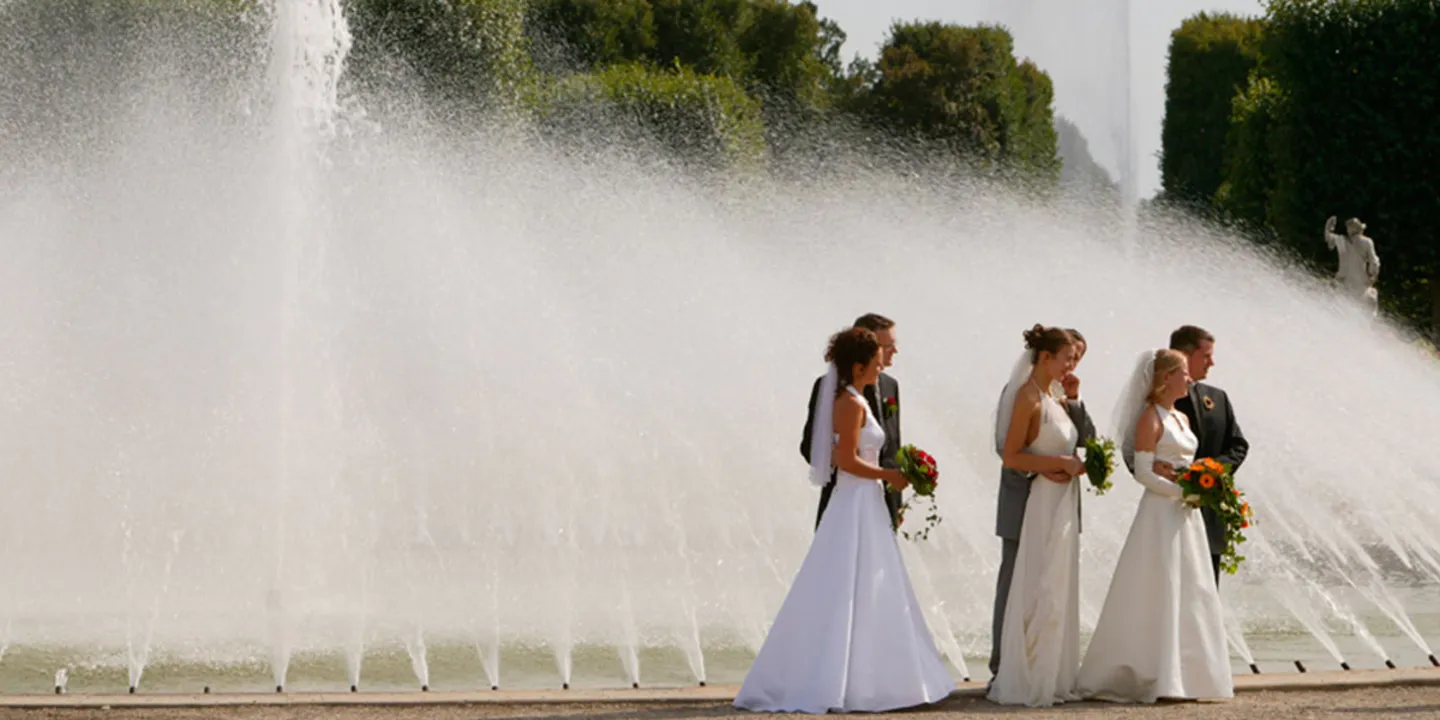 Drei Brautpaare vor einem großen Springbrunnen in den Herrenhäuser Gärten