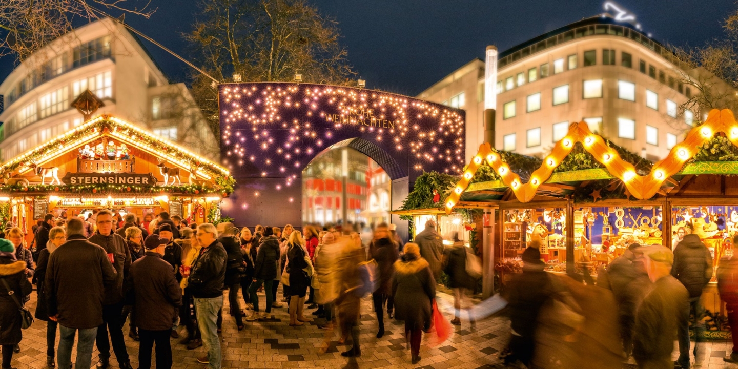 Menschen vor Weihnachtsmarktbuden und einem großen Eingangstor