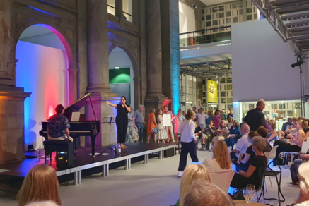 Eine Sängerin und ein Pianist stehen vor Publikum auf einer Bühne im Museum August Kestner